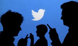 Pessoas no celular com a logo do twitter atrás